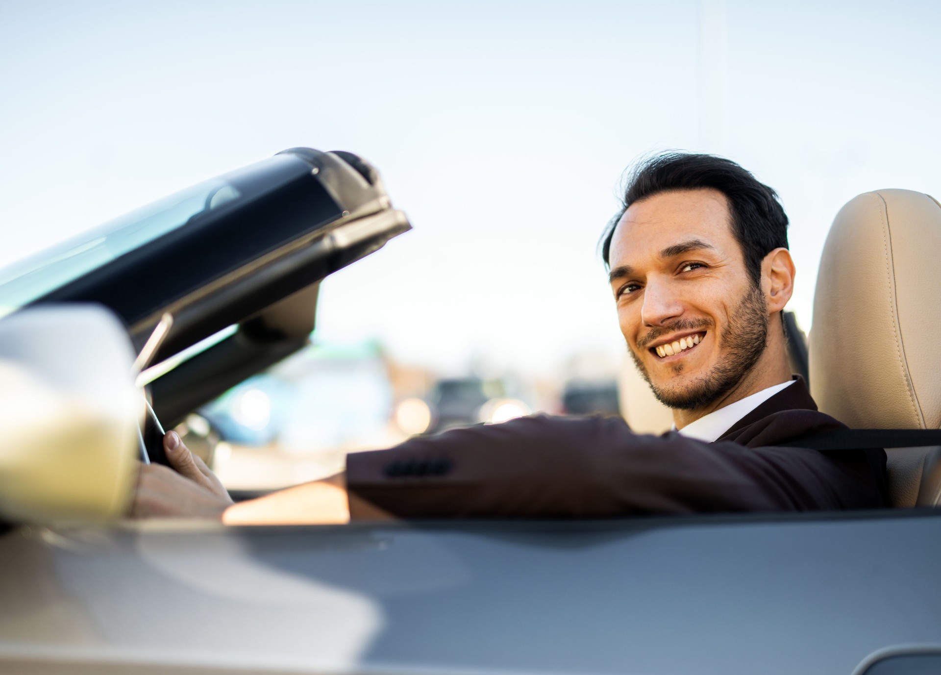 Businessman driving his convertible car smiling at camera